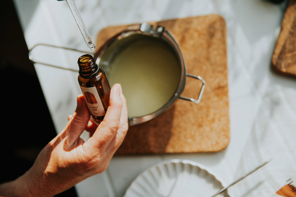 Hands pouring House of EQ oils into melted soy wax pot